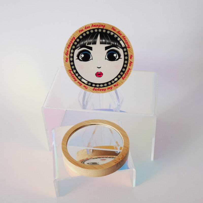 “You Are Amazing” bamboo pocket mirror featuring O’s face and retro lettering around the frame.