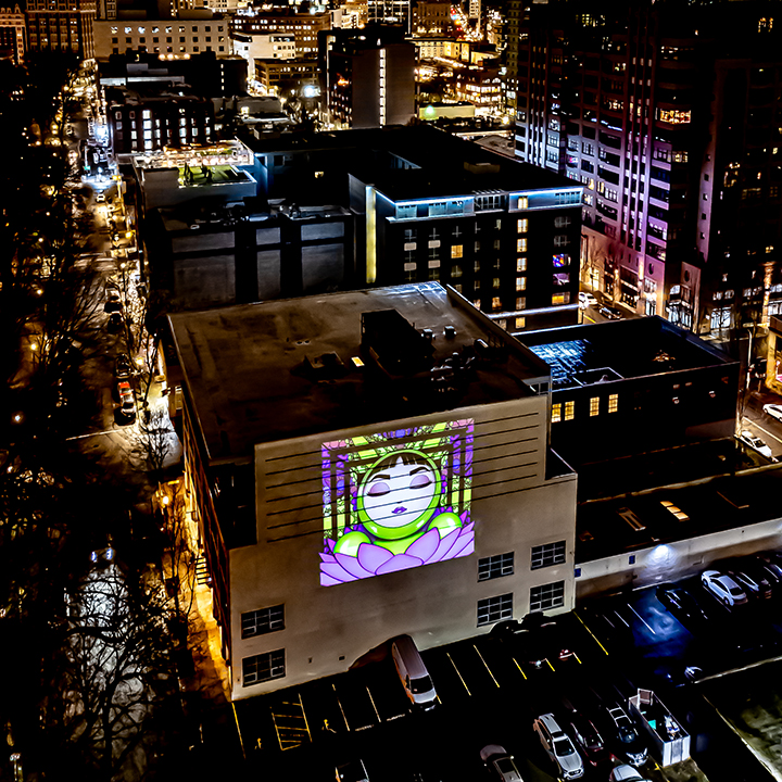 Character-based street art by Alla K projected on a building in Seattle, Washington – featuring O in a glowing, surreal presentation