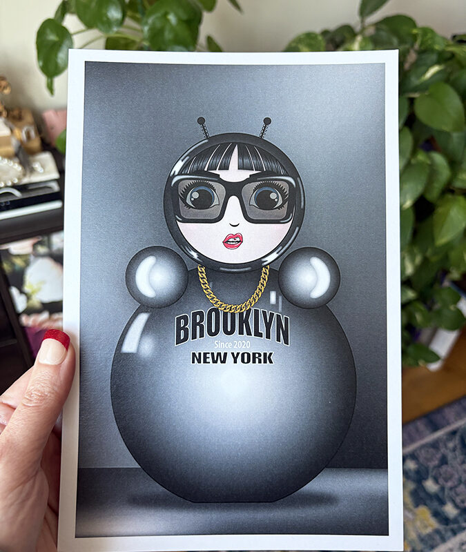 Monochrome O mini art print held in hand, featuring the glossy silver O character with sunglasses, gold chain, and “Brooklyn New York” text.