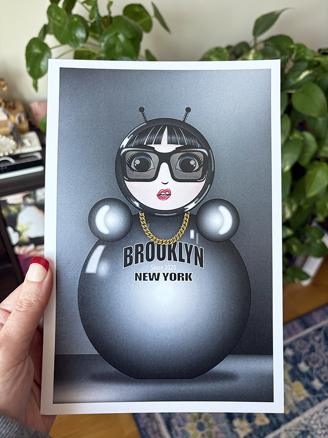 Monochrome O mini art print held in hand, featuring the glossy silver O character with sunglasses, gold chain, and “Brooklyn New York” text.