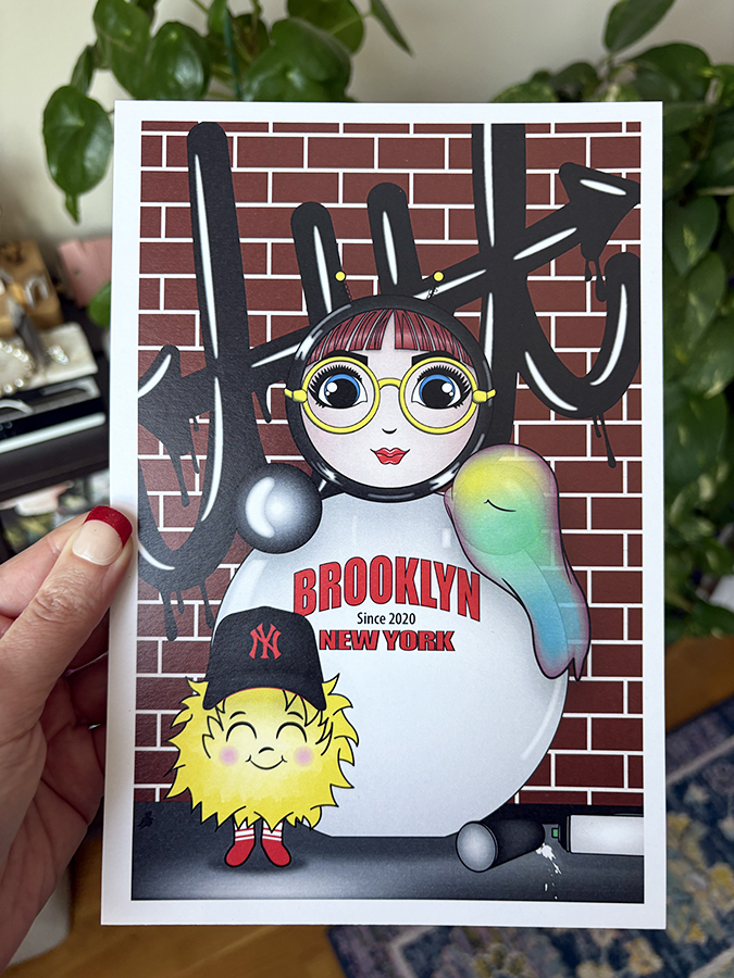 Brooklyn graffiti mini print held in hand, featuring O with yellow glasses and EM in a Yankees hat against a brick wall with black graffiti.