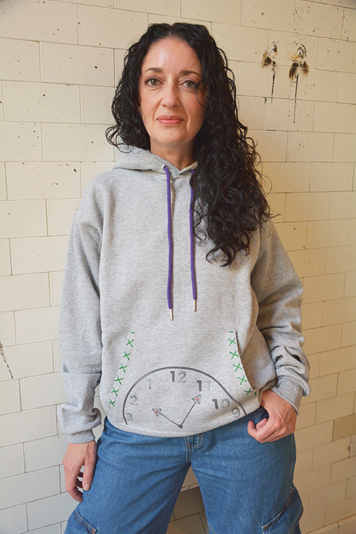 Front view of the gray “Centering Please Hold” sweatshirt with a clock pocket design and purple drawstrings.
